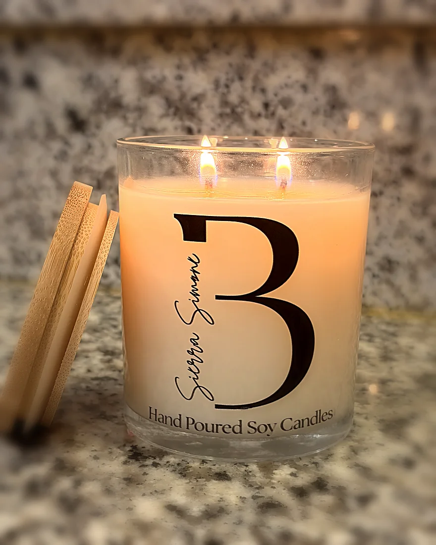 A lit two-wick B. Sierra Simone soy candle with its bamboo lid resting against the jar